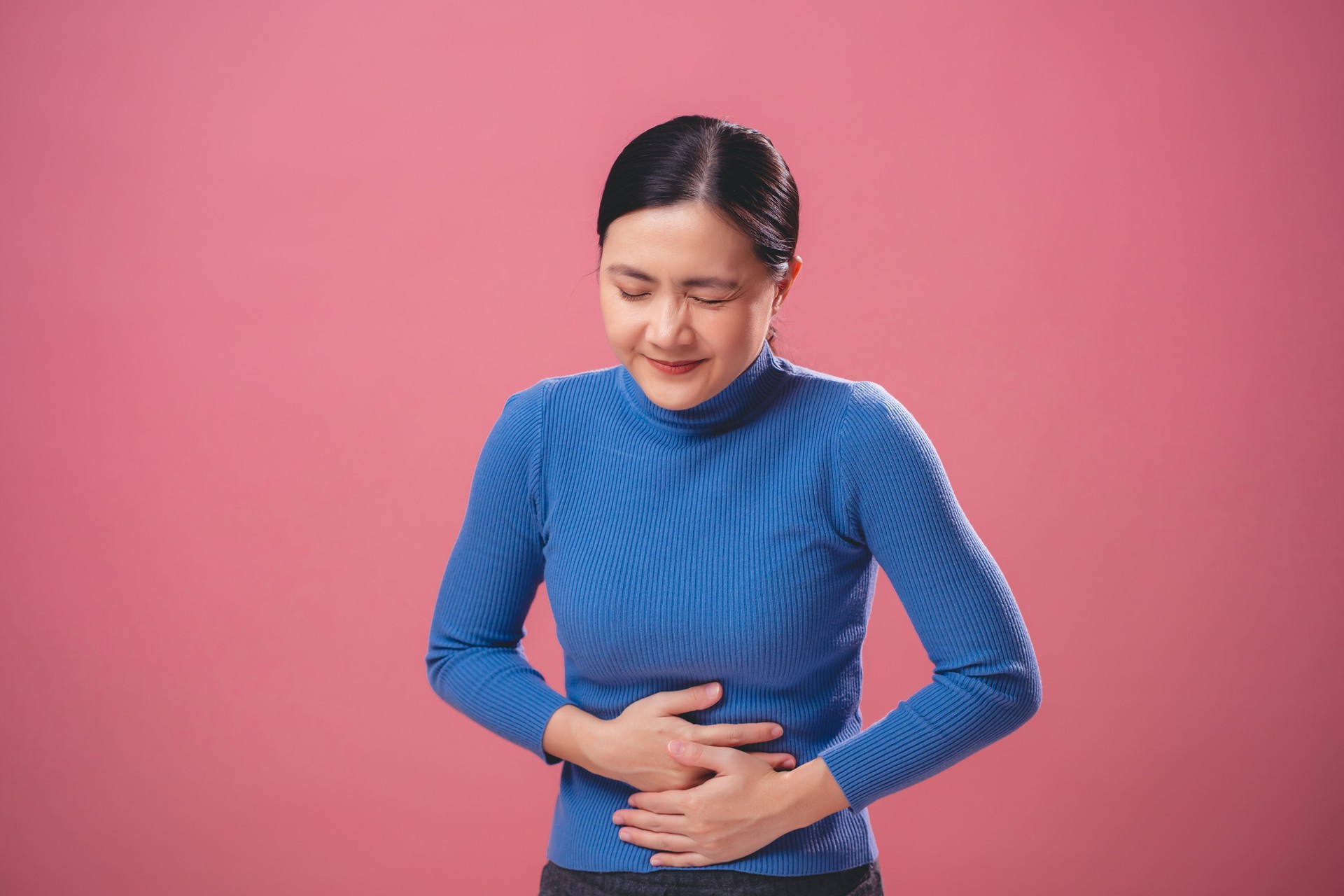 Asian woman was sick with stomach ache standing isolated on pink background.